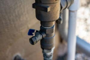 Close-up of a metal outdoor water valve with a blue handle, mounted on a pipe next to a wall—a key component for Winter Irrigation in North Texas.