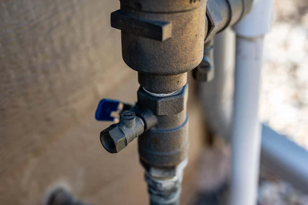 Close-up of a metal outdoor water valve with a blue handle, mounted on a pipe next to a wall—a key component for Winter Irrigation in North Texas.